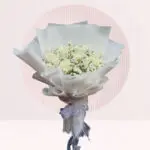 A hand bouquet of white roses and baby’s breath arranged elegantly on a table.