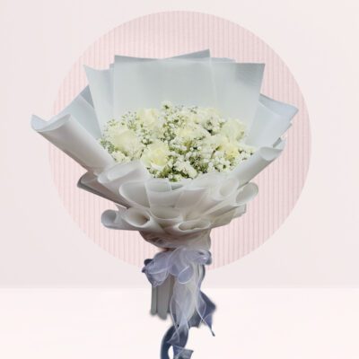 A hand bouquet of white roses and baby’s breath arranged elegantly on a table.