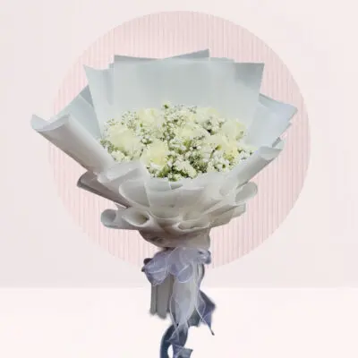 A hand bouquet of white roses and baby’s breath arranged elegantly on a table.