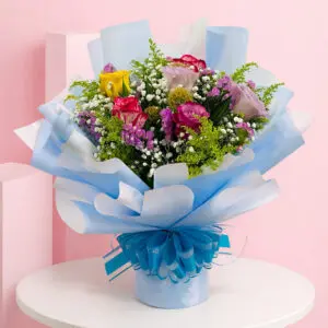 Beautiful hand bouquet with a blue wrap and bow, showcasing a mix of roses, lilies, and hydrangeas in vibrant colors.
