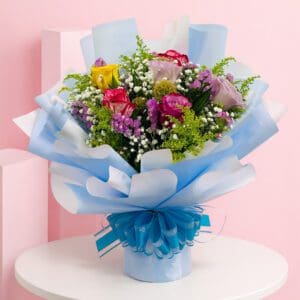 Beautiful hand bouquet with a blue wrap and bow, showcasing a mix of roses, lilies, and hydrangeas in vibrant colors.