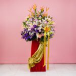A vibrant flower arrangement featuring Eustoma, Hydrangea, and Orchids on a red pedestal for a grand opening display.