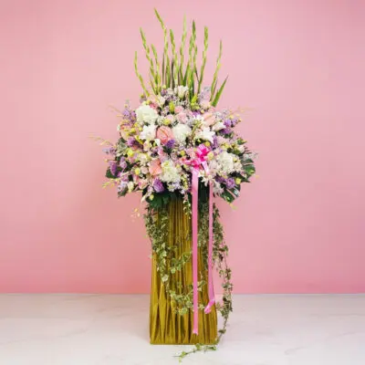 A grand opening stand featuring a tall vase of colorful flowers, including Eustoma and Orchids, set against a pink wall.