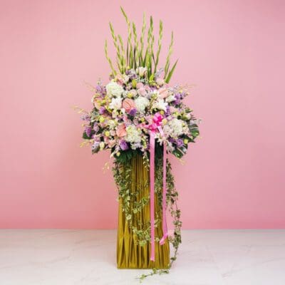 A grand opening stand featuring a tall vase of colorful flowers, including Eustoma and Orchids, set against a pink wall.