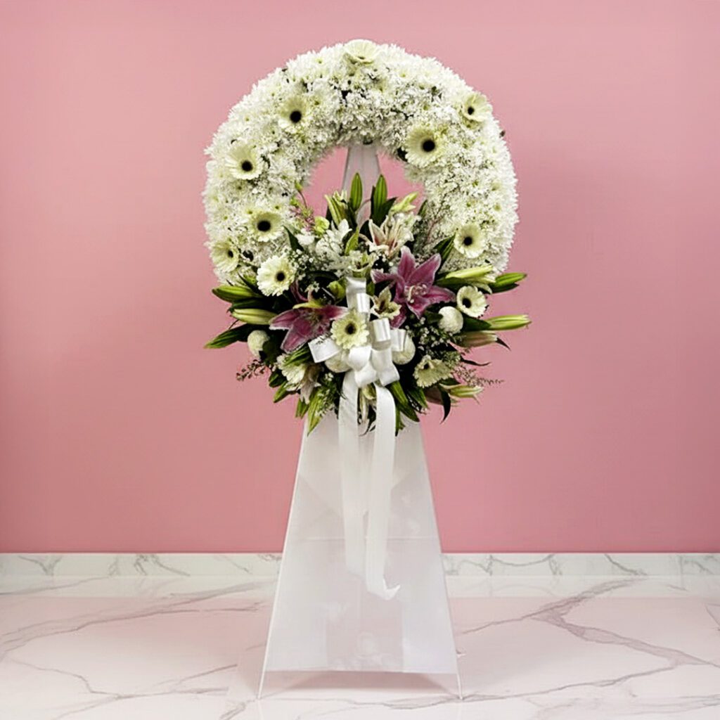 A white floral wreath adorned with colorful flowers and a delicate ribbon
