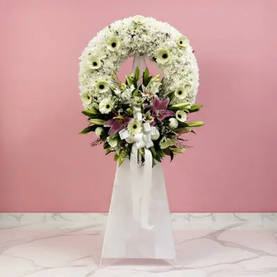 A white floral wreath adorned with colorful flowers and a delicate ribbon