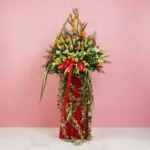 A large floral arrangement featuring 15 roses, 10 lilies, and 5 anthuriums in a red vase for a grand opening stand.