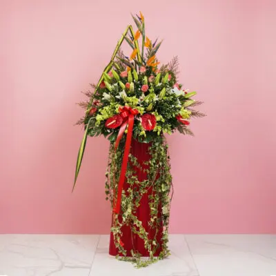A large floral arrangement featuring 15 roses, 10 lilies, and 5 anthuriums in a red vase for a grand opening stand.