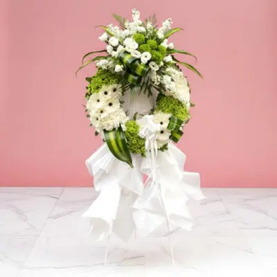 A white floral wreath adorned with white flowers and lush green leaves.