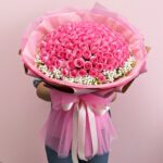 A woman stands holding a large bouquet of pink roses, showcasing their lush blooms and green foliage.