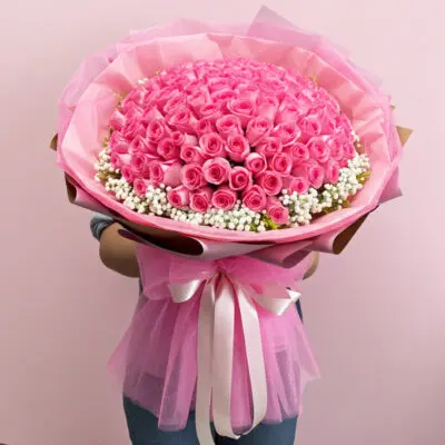 A woman stands holding a large bouquet of pink roses, showcasing their lush blooms and green foliage.