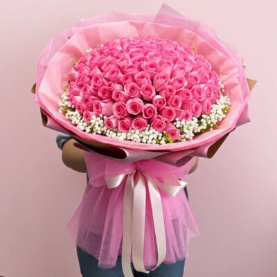 A woman stands holding a large bouquet of pink roses, showcasing their lush blooms and green foliage.