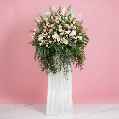 A floral wreath composed of purple and white blooms, elegantly positioned on a stand.