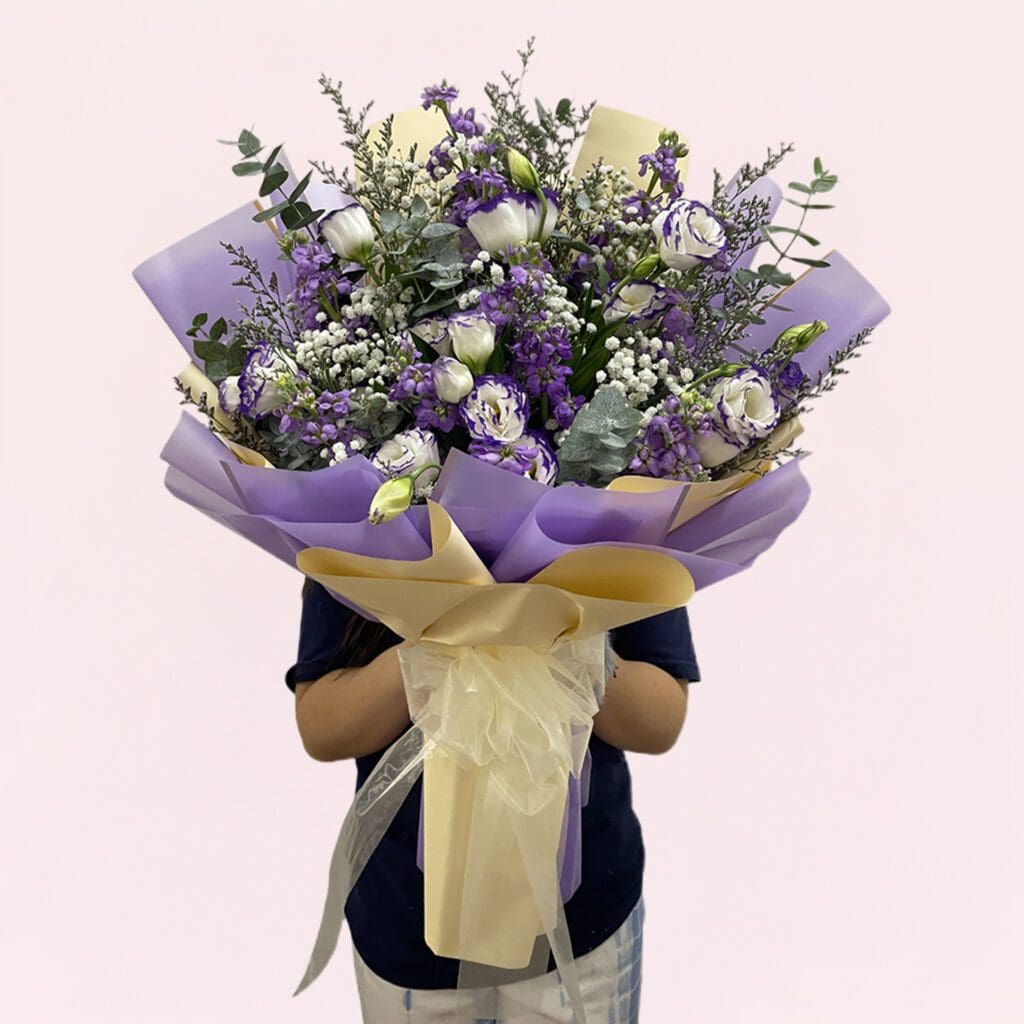 A person holding a bouquet of purple and white flowers, showcasing a mix of blooms and greenery.