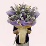 A person holding a bouquet of purple and white flowers, showcasing a mix of blooms and greenery.