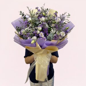 A person holding a bouquet of purple and white flowers, showcasing a mix of blooms and greenery.