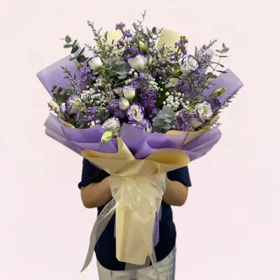 A person holding a bouquet of purple and white flowers, showcasing a mix of blooms and greenery.