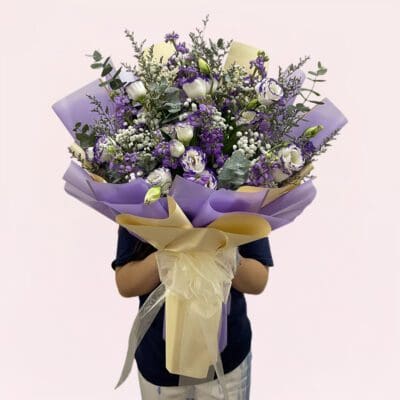 A person holding a bouquet of purple and white flowers, showcasing a mix of blooms and greenery.