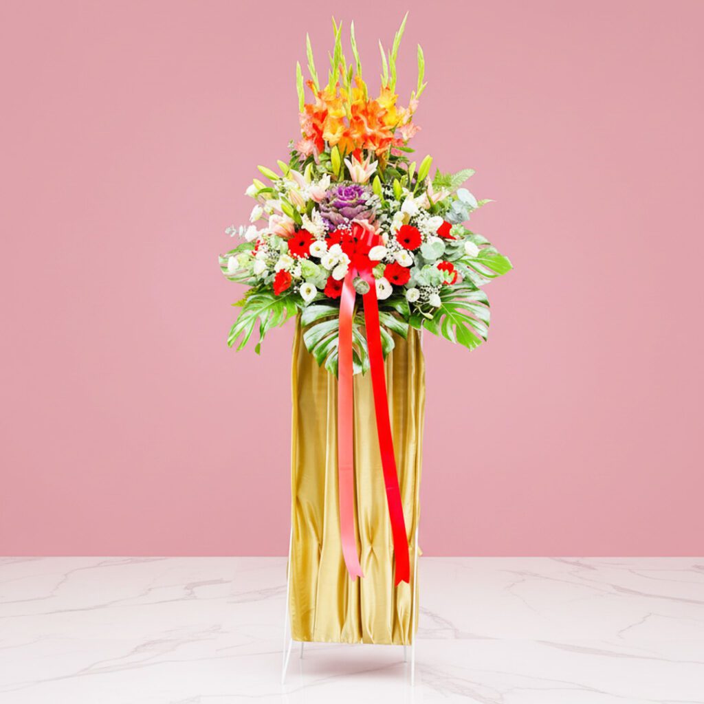A grand opening stand featuring a tall vase with a mix of Gerbera, Eustoma, and Lilies, tied with a ribbon.