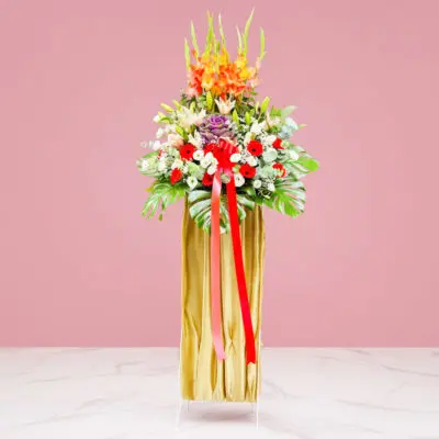 A grand opening stand featuring a tall vase with a mix of Gerbera, Eustoma, and Lilies, tied with a ribbon.