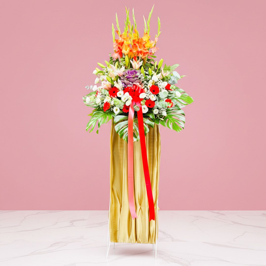 A grand opening stand featuring a tall vase with a mix of Gerbera, Eustoma, and Lilies, tied with a ribbon.