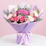 A bouquet of pink and white roses arranged in a purple box, showcasing a vibrant floral display.