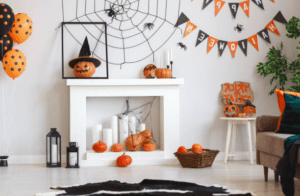 A living room decorated for Halloween with a fireplace filled with pumpkins and candles, a framed pumpkin with a witch's hat, a spiderweb on the wall, and other Halloween decorations