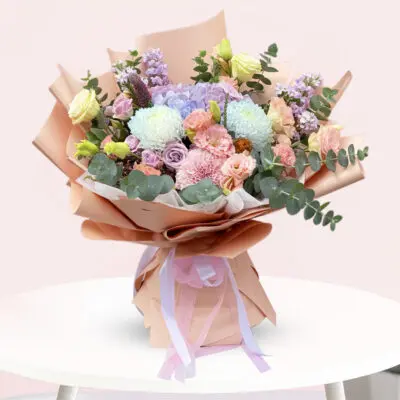 A colorful bouquet of flowers arranged in a paper bag, placed on a wooden table.