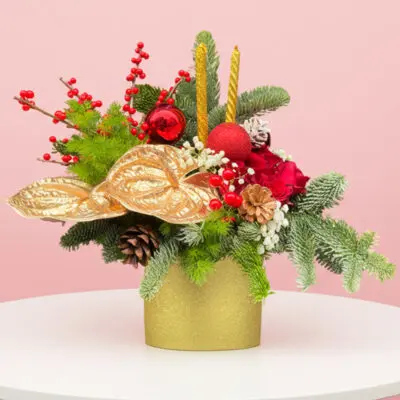A gold vase filled with vibrant red and green flowers alongside lush evergreen branches.