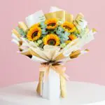 A vibrant bouquet of sunflowers tied with a gold ribbon, showcasing bright yellow petals and lush green leaves.