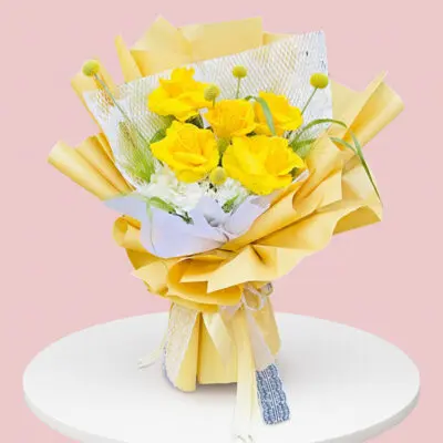 A bouquet of yellow roses arranged on a pink table, showcasing vibrant colors and a cheerful atmosphere.