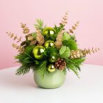 A green vase adorned with gold ornaments and pine cones, designed as a festive Christmas centerpiece.