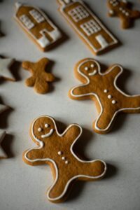 The image shows a variety of gingerbread cookies. There are two gingerbread men, a gingerbread house, and some gingerbread stars. The cookies are decorated with white icing.