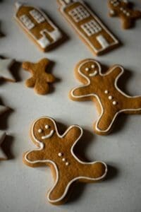 The image shows a variety of gingerbread cookies. There are two gingerbread men, a gingerbread house, and some gingerbread stars. The cookies are decorated with white icing.
