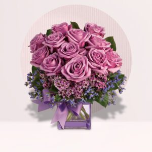 The image shows a beautiful bouquet of purple roses arranged in a glass vase. The roses are a deep shade of purple, and they are accented with smaller purple flowers and greenery. The bouquet is tied with a purple ribbon.