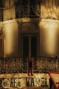 The image focuses on a building decorated with festive lights. The building has a balcony with an intricate wrought iron railing.