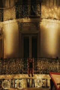 The image focuses on a building decorated with festive lights. The building has a balcony with an intricate wrought iron railing.