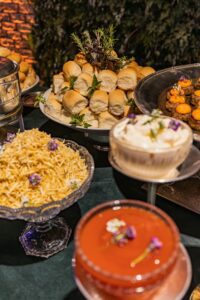 A buffet table with a variety of dishes, including small rolls, potatoes, a dip, and a red sauce.
