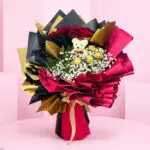 A bouquet featuring a teddy bear adorned with red and black ribbon, creating a charming and playful arrangement.