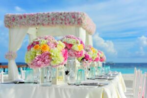 A wedding table setting on a beach with floral centerpieces, glasses, and silverware.