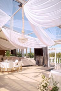 A wedding venue with a glass ceiling and white drapes hanging from it.