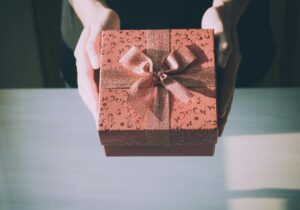 Red gift box with a gold geometric pattern and a tied gold ribbon, held in two hands.