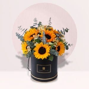 A bouquet of sunflowers and other flowers in a round black box with gold trim