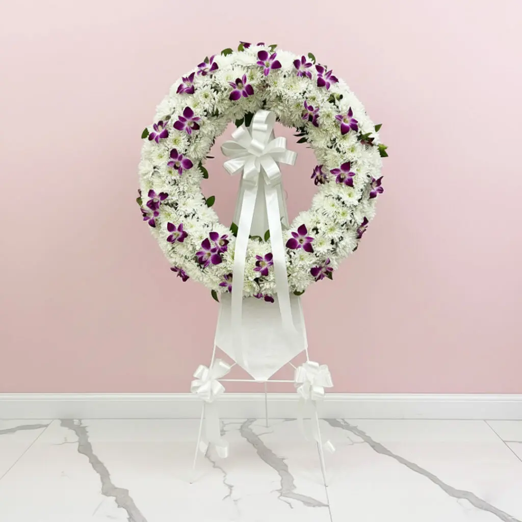 A floral wreath composed of purple and white blooms, elegantly positioned on a stand.