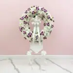 A floral wreath composed of purple and white blooms, elegantly positioned on a stand.