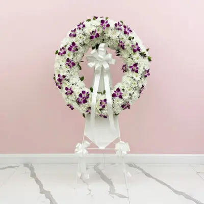 A floral wreath composed of purple and white blooms, elegantly positioned on a stand.