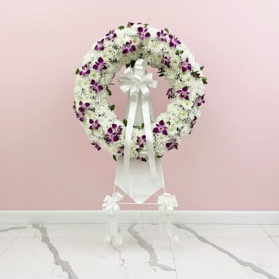 A floral wreath composed of purple and white blooms, elegantly positioned on a stand.