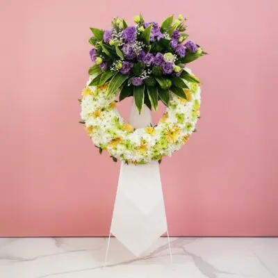A floral wreath composed of purple and white blooms, elegantly positioned on a stand.