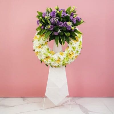 A floral wreath composed of purple and white blooms, elegantly positioned on a stand.