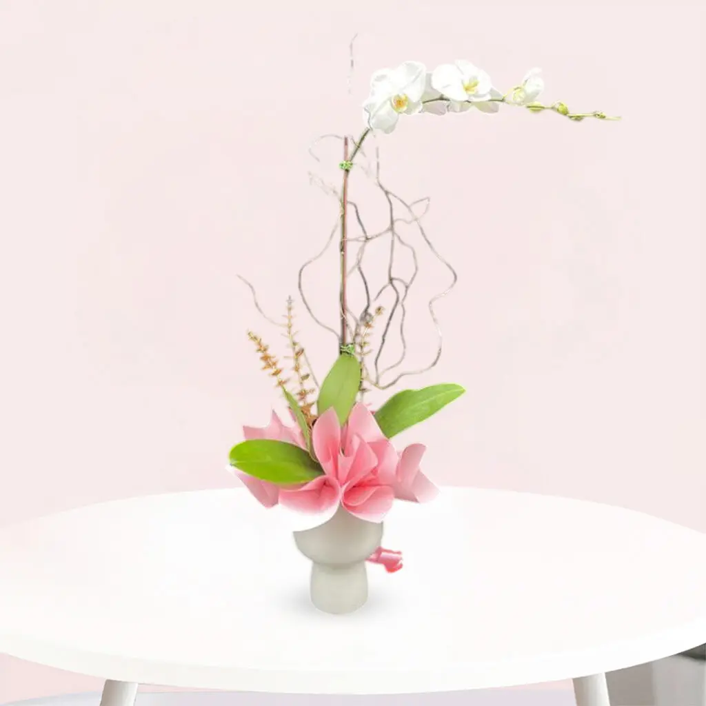 A vase filled with white orchid and pink flowers sits elegantly on a wooden table.